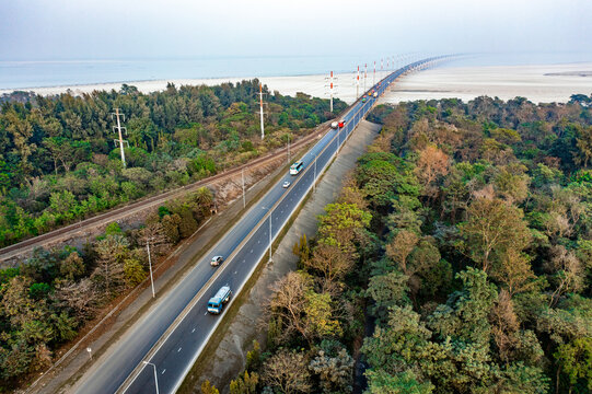 Aerial view of Jamuna Bridge with vehicles on the highway and a parallel railway track surrounded by lush green forest in Tangail District, Dhaka Division, Bangladesh.