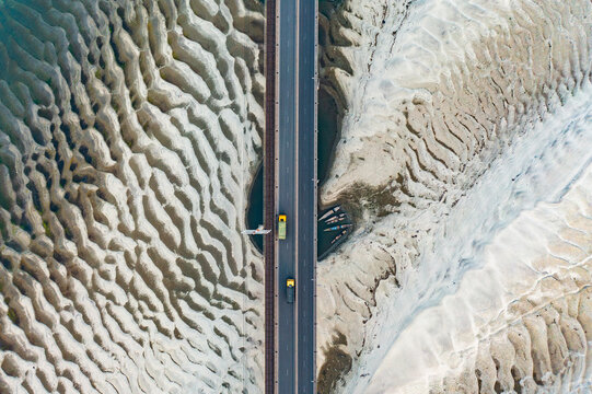 Aerial view of Jamuna Bridge crossing over a textured sandy riverbed with ripple patterns and trucks driving on the road in Tangail District, Dhaka Division, Bangladesh.