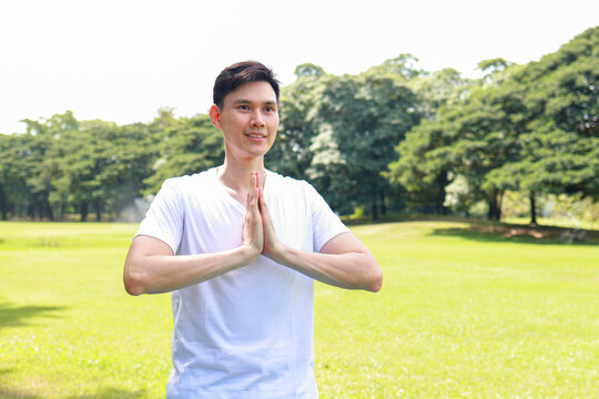 A healthy young Asian man is practicing yoga and meditation poses on an outdoor lawn. Healthy lifestyle, exercise, and self-care.