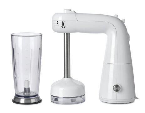 A white, handheld kitchen appliance with an immersion blending wand and a tall, clear plastic beaker sits on a white surface