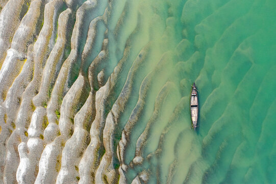 Aerial view of a wooden boat floating near the wavy sandbars of the Jamuna River Char in Tangail District, Dhaka Division, Bangladesh.