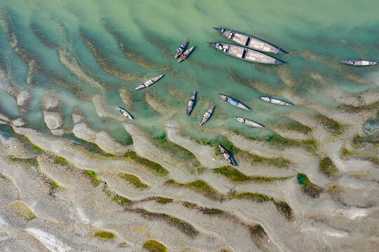 Aerial view of wooden boats moored along the sandy banks and sandbars of the Jamuna River Char in Tangail District, Dhaka Division, Bangladesh.