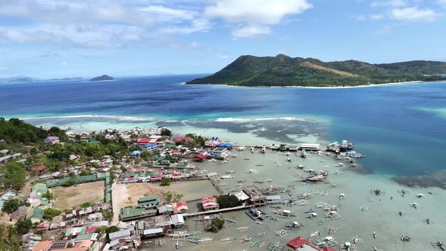 Aerial view of tropical island village with boats docked in clear blue ocean waters.