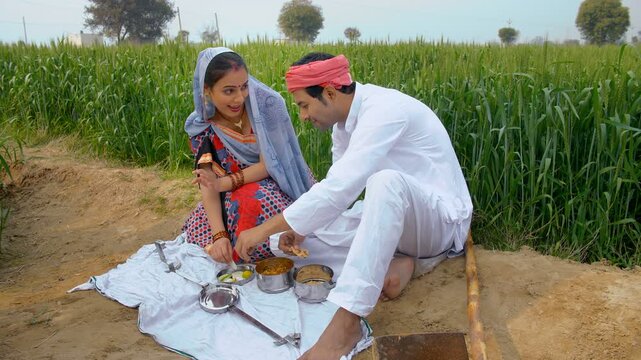 Happy village couple having food together during a break from agricultural work. Medium shot of an Indian farmer and his wife eating lunch after a day's hard work in their farmland - village lifestyle