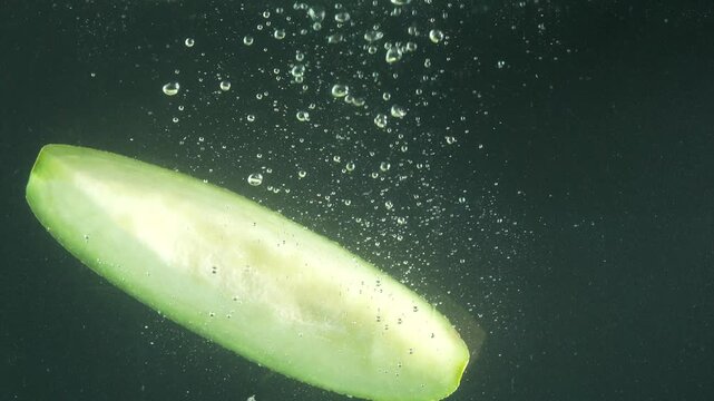 A melon slice drops into water, splashing and creating many bubbles