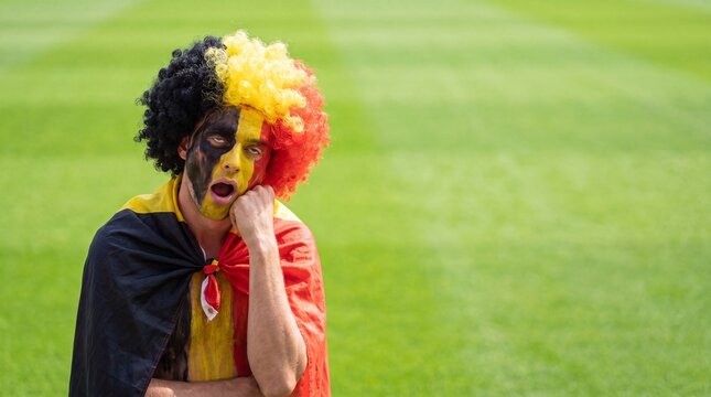 A bored Belgian football fan with face paint and a wig sits dejectedly in an empty stadium