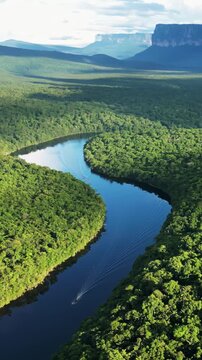 Aerial view of a boat cruising down a winding tropical river with tepui mountains in the background.
