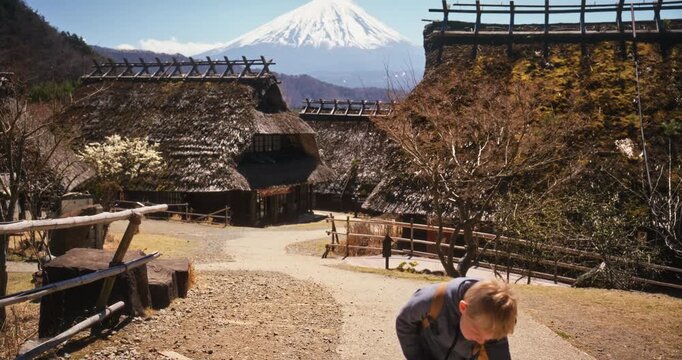 Boy with backpack running through old Japanese village with Mt. Fuji in the background - wide shot