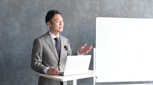 グレー背景でプレゼンをするスーツを着た日本人男性