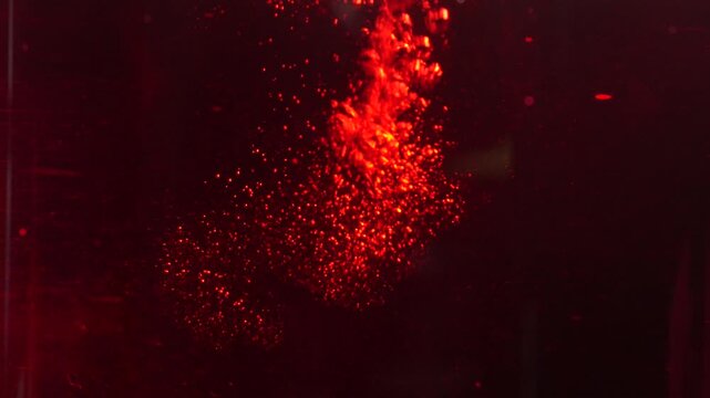 Stream of glowing red bubbles rising in dark liquid macro abstract. Deep crimson fluid with sparkling effervescence and textured motion.