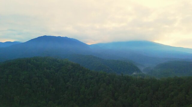 Aerial view of the misty mountain peaks and dense tropical forests during a soft sunset in Sukabumi, West Java, Indonesia.