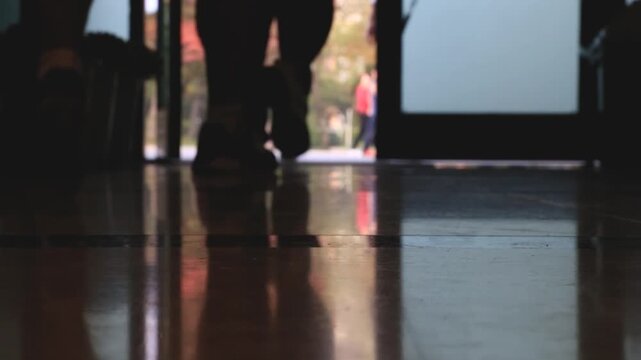사람 스포츠 훈련 코트 야외 일상 소품 디테일 자재: 어두운 실내 바닥에 비친 반영 너머로 사람들이 밝은 야외 문밖으로 걸어나가는 로우앵글 동영상 클립입니다.