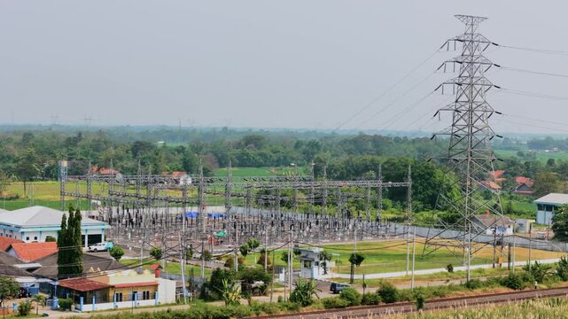 Aerial view of an electrical substation with high-voltage transmission towers and power lines surrounded by lush greenery and houses in Pekalongan, Central Java, Indonesia.