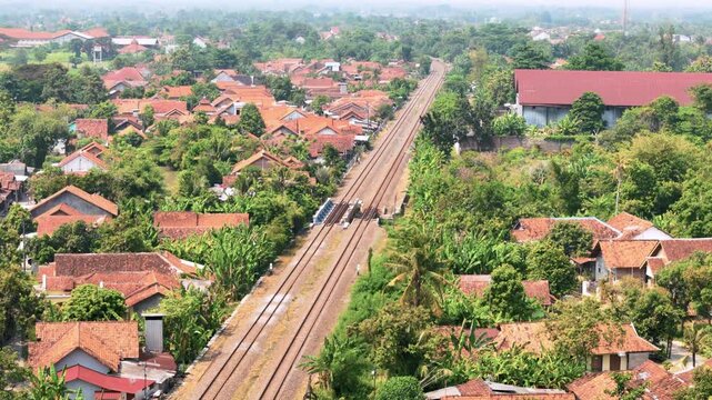 Aerial view of railway tracks passing through a residential neighborhood with orange rooftops and lush greenery in Pekalongan, Central Java, Indonesia.