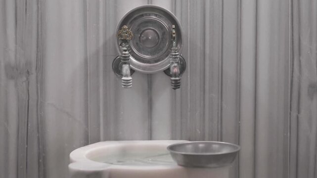 Clear water flows from classic brass taps into a kurna (marble basin), complete with a floating metal bowl (bag) used for washing.