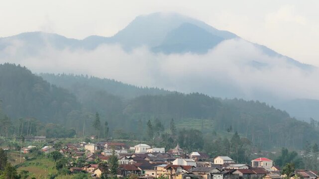 Aerial view of a rural village nestled at the foot of misty mountains with lush green forests under a cloudy sky Pekalongan, Central Java, Indonesia.
