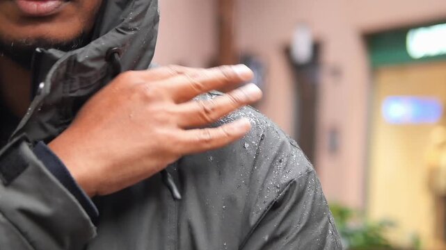 a man wearing a dark waterproof windbreaker jacket in the rain. removing water drops from jacket
