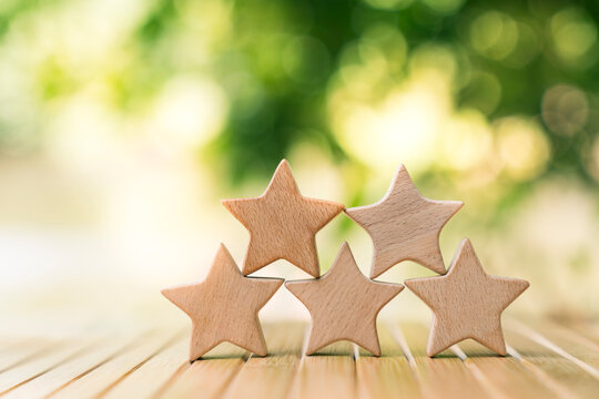 Five wooden star shape models on table with green nature bokeh background. Concept of excellent customer service rating, top quality review, business satisfaction, and premium performance.