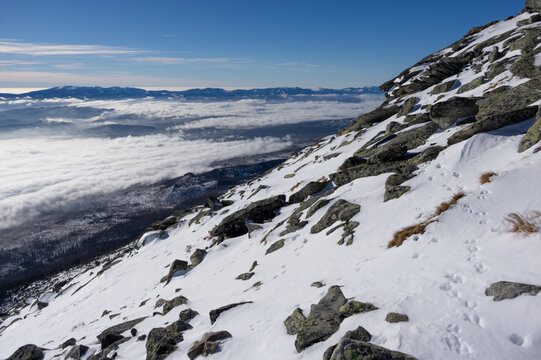 View of Slavkovsky nos mountain peak with snowy slopes and rocky terrain overlooking a sea of clouds in the valley under a clear blue sky Vysoke Tatry, Presov Region, Slovakia.