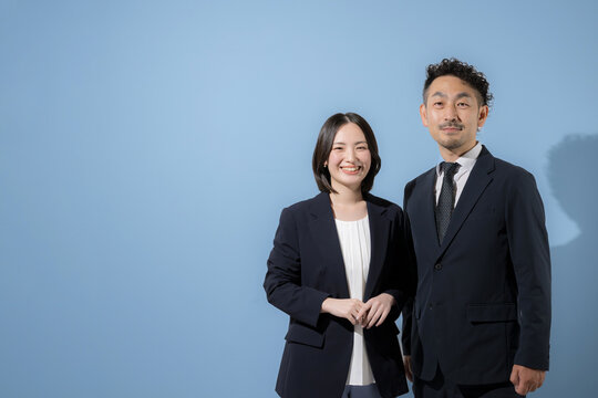 水色背景でカメラ目線のスーツのビジネスマン男女　笑顔でリーダーシップや成功やチャレンジのbtobイメージ　左にコピースぺースあり