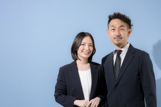 水色背景でカメラ目線のスーツのビジネスマン男女　笑顔でリーダーシップや成功やチャレンジのbtobイメージ　左にコピースぺースあり