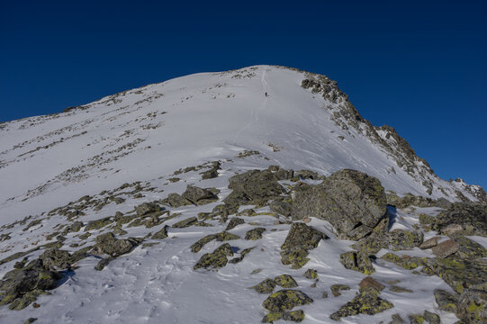 View of Slavkovsky nos mountain peak with snow-covered slopes and rocky terrain under a clear blue sky with a lone hiker on the trail Vysoke Tatry, Presov Region, Slovakia.