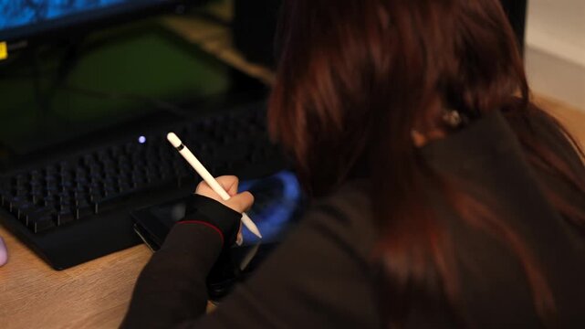 Young digital artist working on tablet screen with stylus pen at desk.