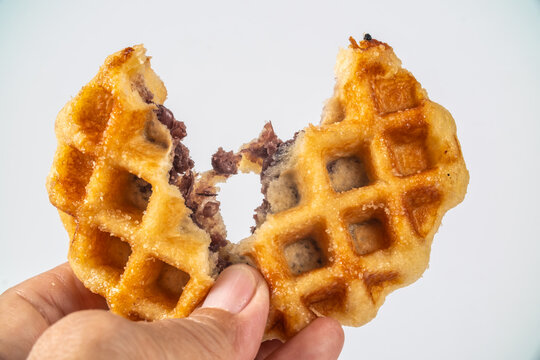 A Belgian waffle in your hand, coated in sugar and filled with sweet red bean paste, perfect for breakfast or as a snack. Image on white background.