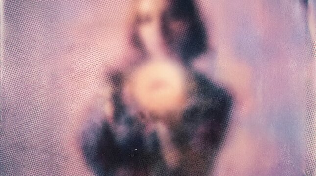 A blurry, ethereal image of a figure holding a glowing orb, surrounded by soft purple and pink hues, evoking a mystical or spiritual atmosphere.
