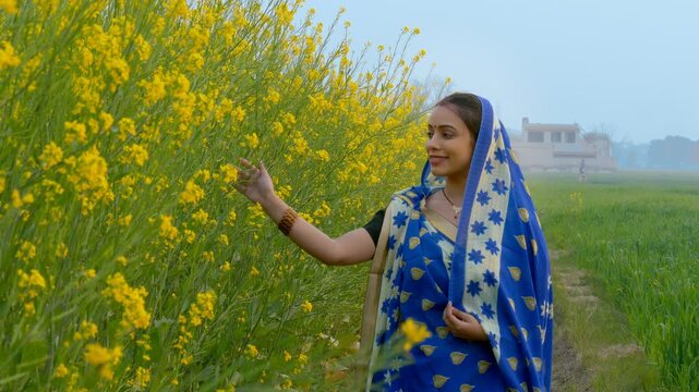 Portrait of a married village woman enjoying in her mustard (Sarso) field. Medium shot of a happy Indian lady in a traditional saree spending time in her agricultural field - village lifestyle concept