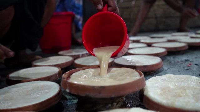 Bogura, Bangladesh - 02 June 2026: View of a worker pouring milk into clay pots to prepare traditional Bogura Doi yogurt in a local workshop.