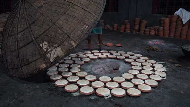 Bogura, Bangladesh - 02 June 2026: View of traditional curd making with a worker lifting a large bamboo dome to reveal rows of clay pots in a workshop in Bogura, Rajshahi Division.