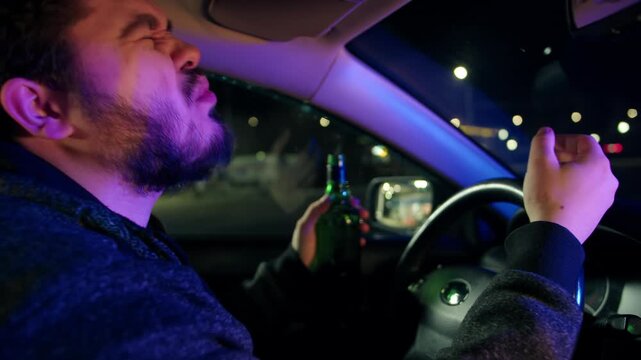 Portrait of raged bearded drunk man who sits with a bottle behind the wheel of a car and was caught by the police for drunk driving at night. Police lights illuminate the frustrated expression