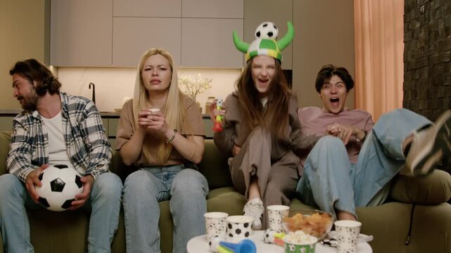 Group of young adults watching soccer match on couch, displaying various emotions with soccer balls and snacks in a cozy living room setting