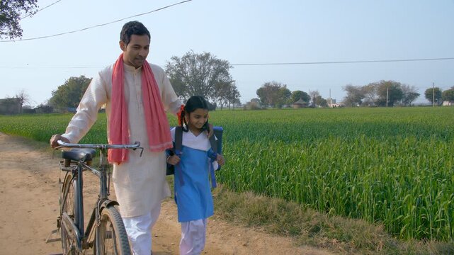 A young village farmer taking his girl child to school. Beti bachao beti padhao. An Indian father and his school-age daughter in uniform - walking on a mud road. Girl child education