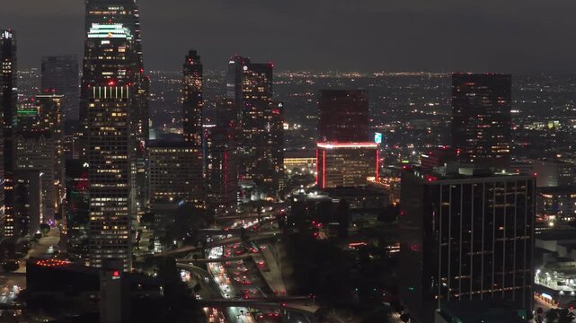 Mesmerizing elevated sight of downtown Los Angeles at night, glowing skyscrapers and office buildings define city's skyline with car traffic on the highway