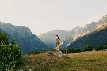 Obraz premium A woman hiking along a grassy trail in a mountain landscape, embracing outdoor solitude and the refreshing air of nature. The scene suggests calm and wellness on the move.