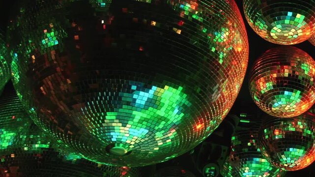 Numerous mirrored disco balls spin slowly, casting a dazzling array of vibrant, kaleidoscopic light patterns across a dark room during a festive evening celebration.