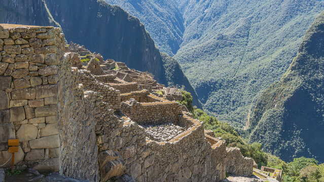Ancient Lost City of the Incas Machu Picchu. Ruins of stone buildings on a mountainside. Dilapidated masonry walls, stairs, terraces. People are walking. The background is mountain slopes. Peru. Cusco