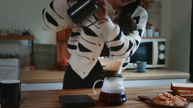 Woman carefully pouring hot water into a dripper with coffee grounds. Morning routine making pour-over coffee for breakfast at home kitchen