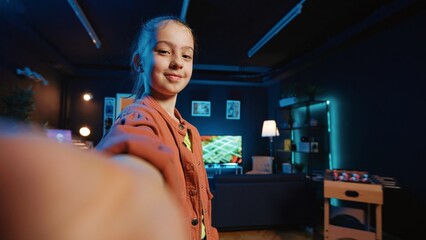 Kid films POV style dance tutorial video with smartphone in blue neon lit living room. Young dancer does viral online social media dancing challenge, capturing footage with selfie cellphone camera