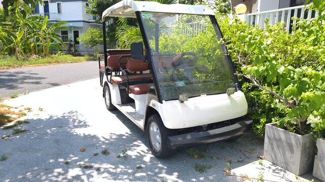 Eco vehicle presented by white electric golf cart is parked in tropical resort. This modern eco vehicle offers clean green transportation on sunny paths near luxury villas and gardens.