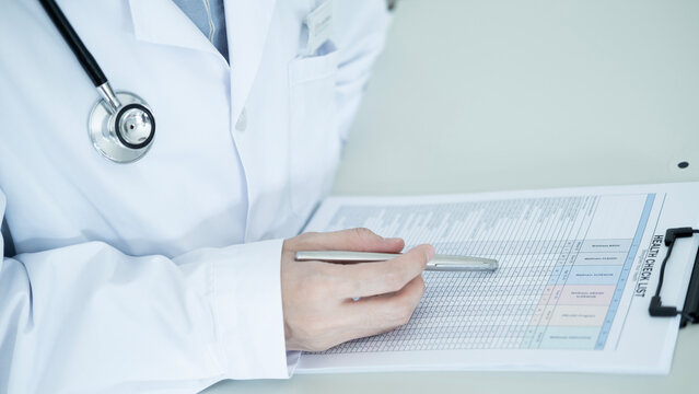 Healthcare professional writing on a health checklist form with stethoscope in clinic, medical checkup, patient record and preventive care concept.