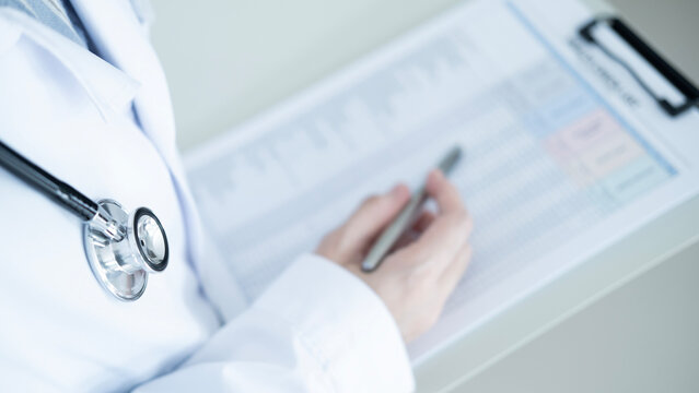 Close up of stethoscope and hand holding pen over health check form, medical checkup paperwork and healthcare assessment concept.