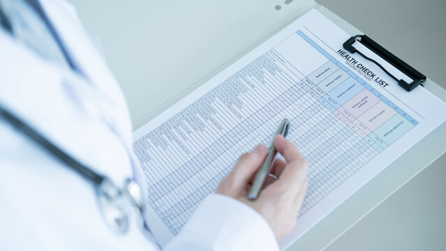 Doctor completing health checklist on clipboard in hospital clinic, medical examination, wellness screening and patient care documentation concept.