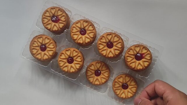 Top down view of a full clear plastic packaging tray loaded with sweet jam-filled cookies on a white background, commercial bakery product showcase