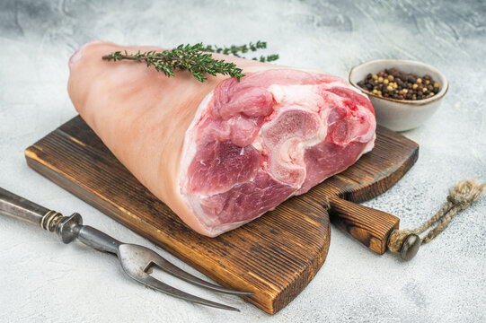 Raw pork knuckle with thyme and pepper on wooden board vertical top view perfect for cooking guides butchery and culinary stock content.