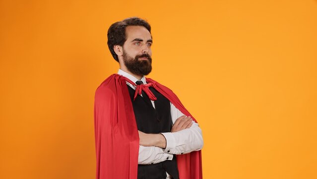 Powerful fantasy hero with red cape standing against yellow background, feeling determined and confident on camera. Dedicated butler acting like superhero, staff member having mantle.