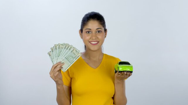 Portrait of a cheerful smiling girl with money and a model of her dream car. Medium shot of an ambitious smart businesswoman saving money to buy a luxury car - financial planning