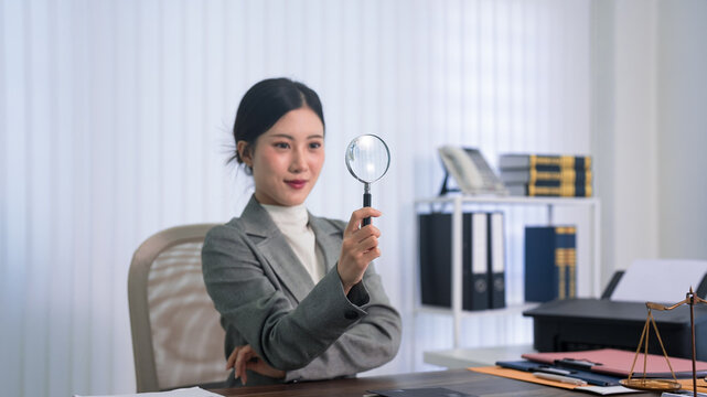 Asian lawyer professional holding magnifying glass for investigation review document research at law office desk with legal book gavel scale justice
